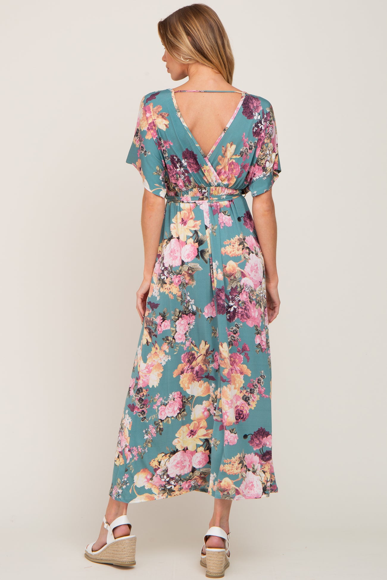 Woman from behind wearing a teal floral maxi dress with a v-back and white wedge sandals