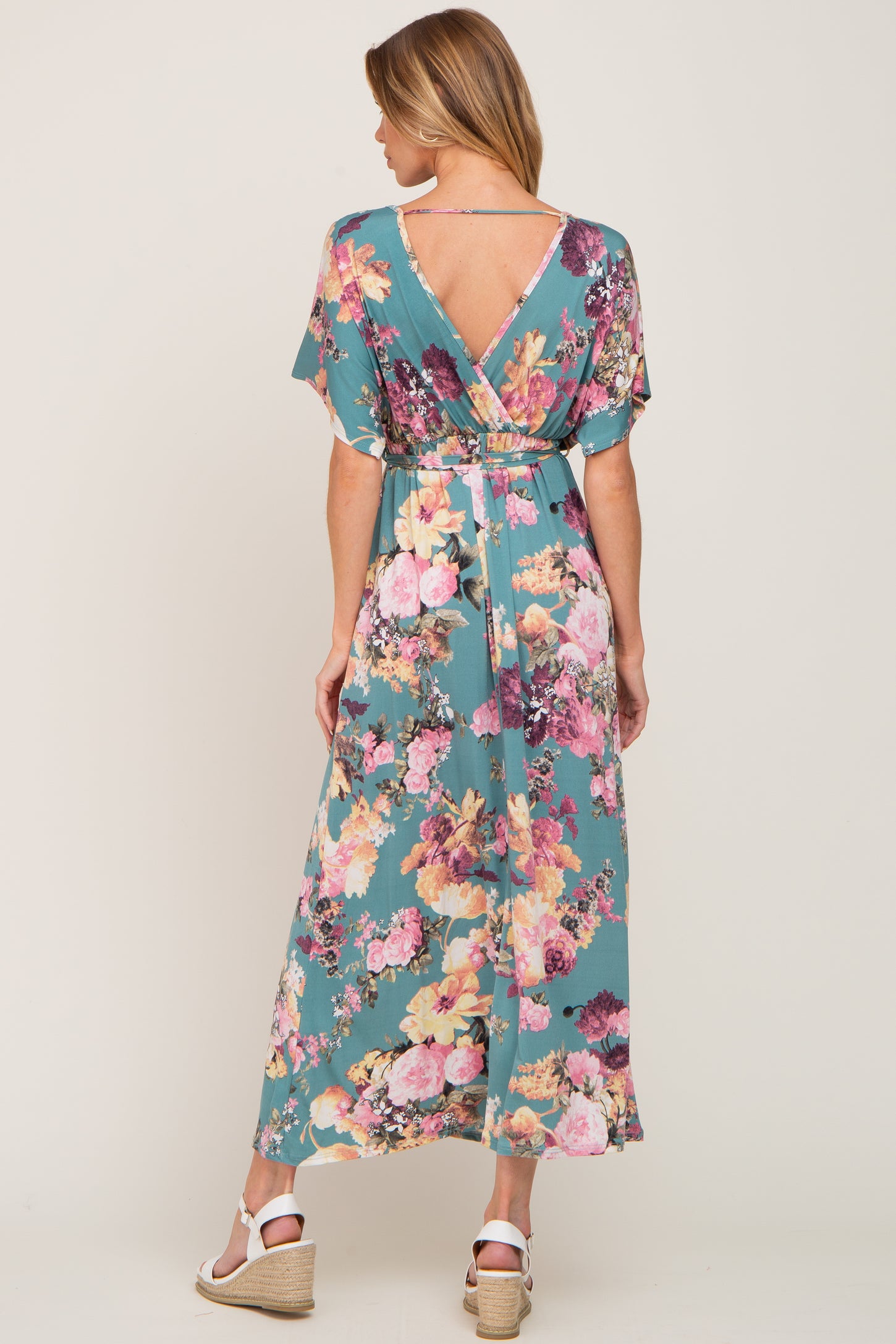 Woman from behind wearing a teal floral maxi dress with a v-back and white wedge sandals