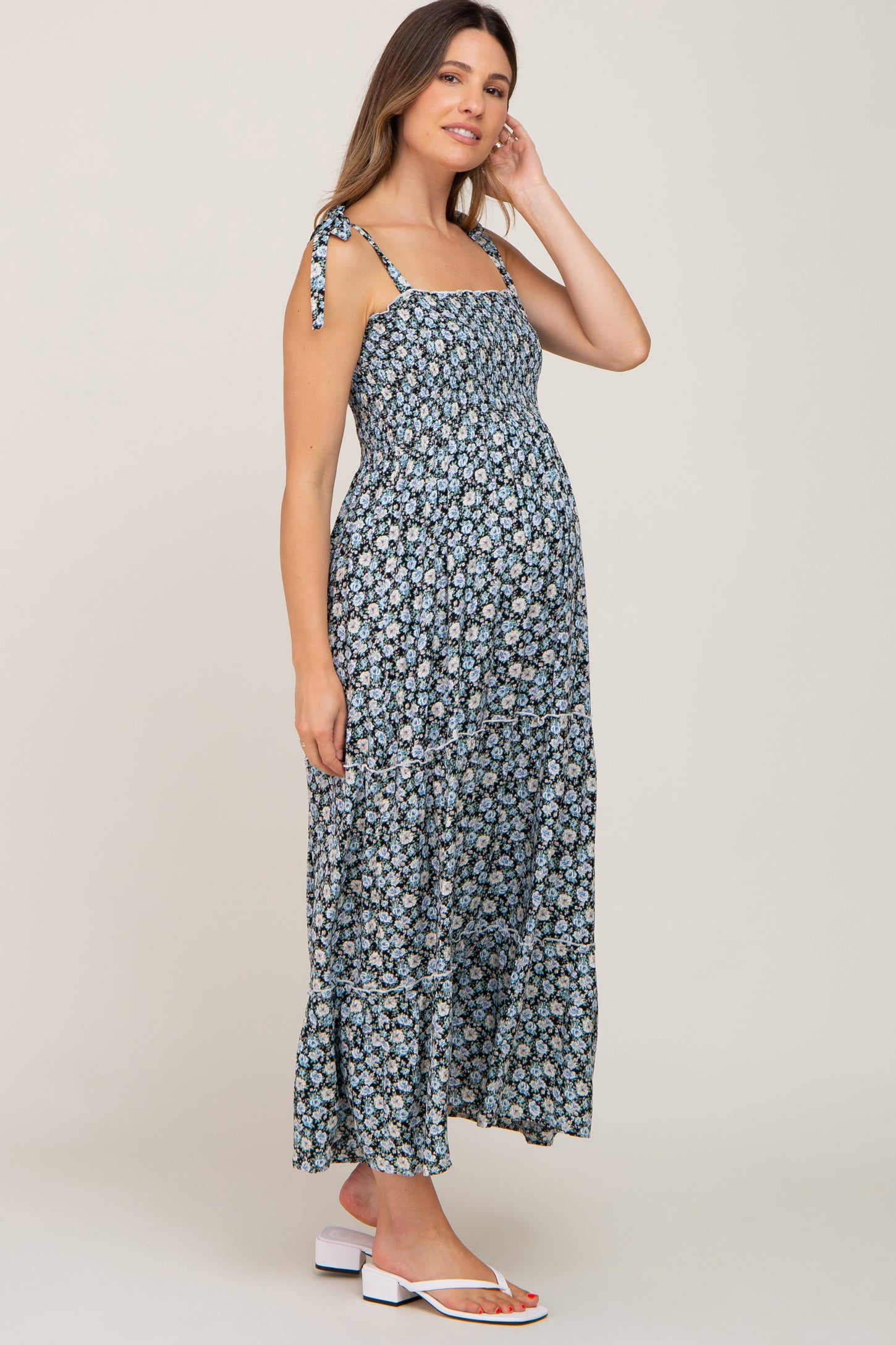 Pregnant woman wearing a blue floral smocked maternity maxi dress with tie straps and tiered skirt
