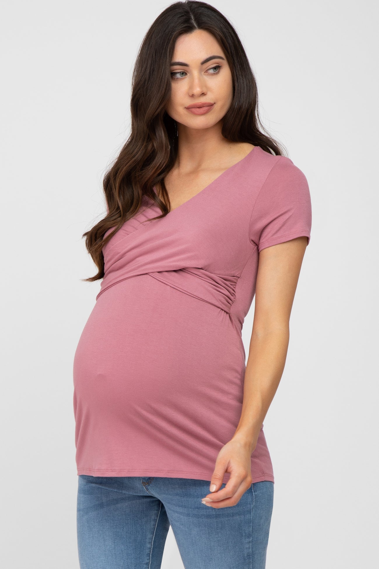 pregnant woman wearing a mauve short sleeve wrap maternity top and blue jeans