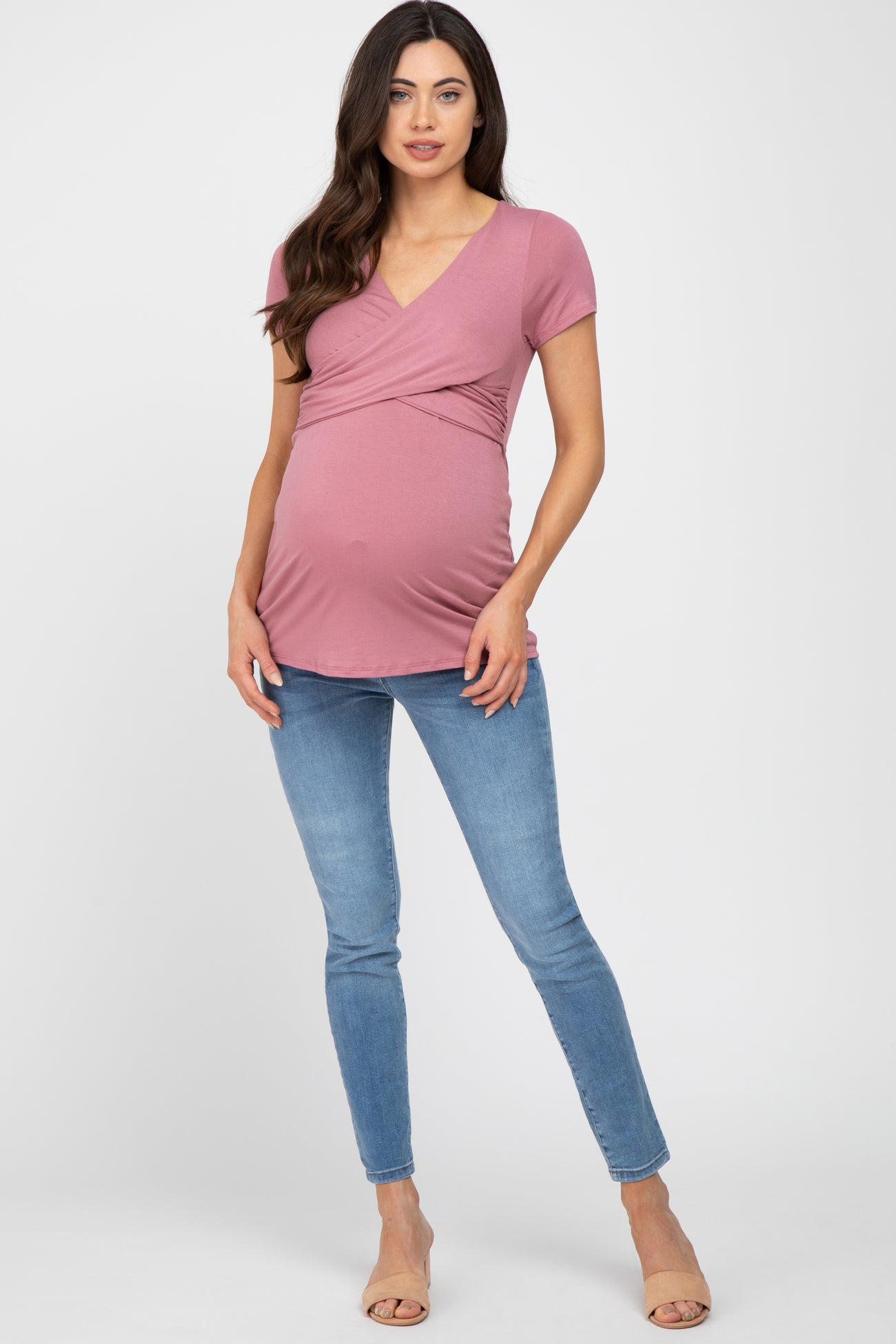 pregnant woman wearing a mauve short sleeve maternity wrap top and blue skinny jeans