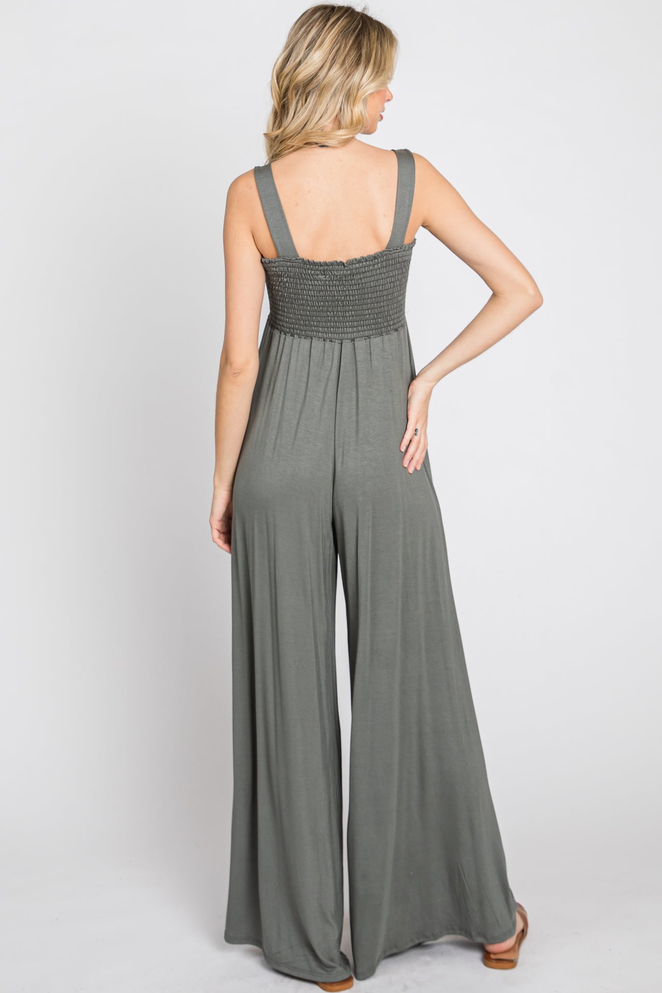 woman wearing a grey smocked back jumpsuit with wide leg pants, viewed from the back