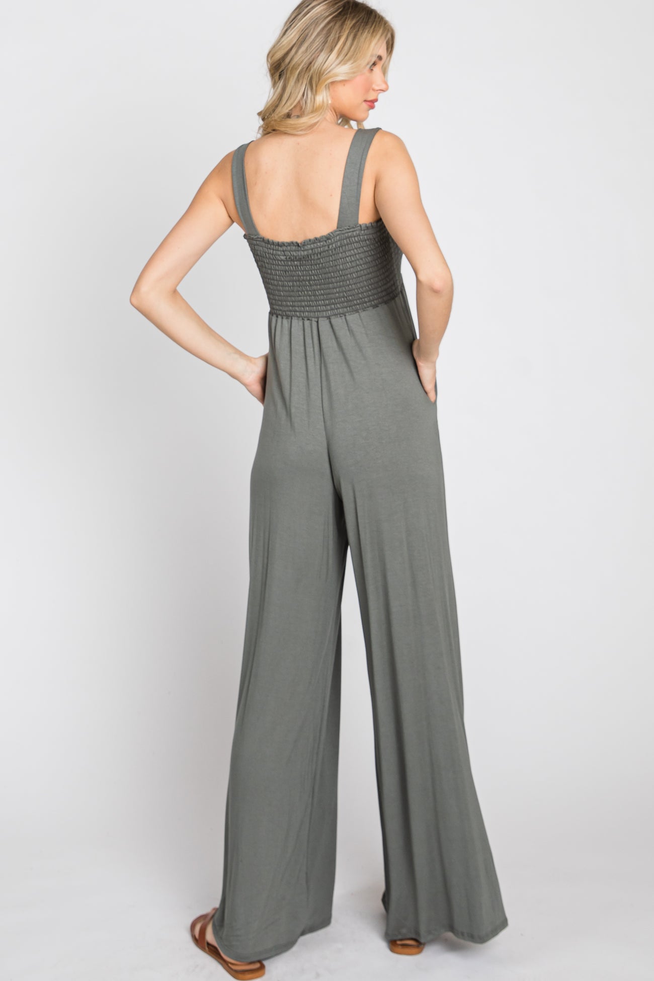 woman wearing a back view of a sage green wide-leg jumpsuit with smocked detailing on the bodice