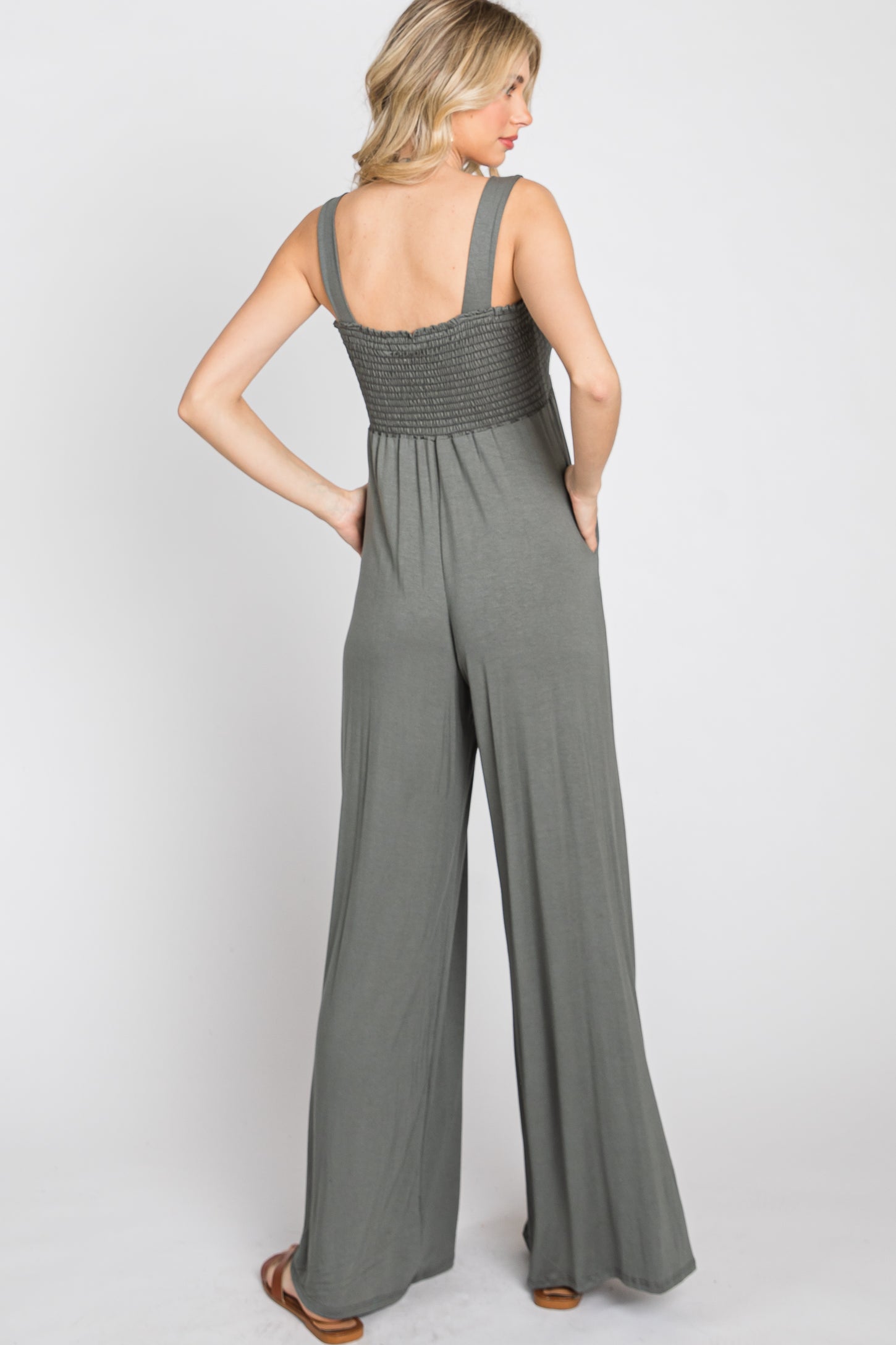 woman wearing a back view of a sage green wide-leg jumpsuit with smocked detailing on the bodice