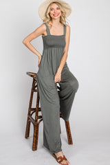 woman wearing a grey sleeveless jumpsuit with a smocked bodice sitting on a stool and wearing a straw hat
