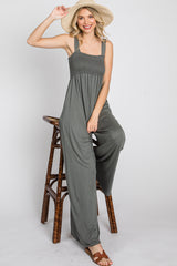 woman wearing a dark gray jumpsuit with a smocked bodice, sitting on a stool and wearing a wide-brimmed hat