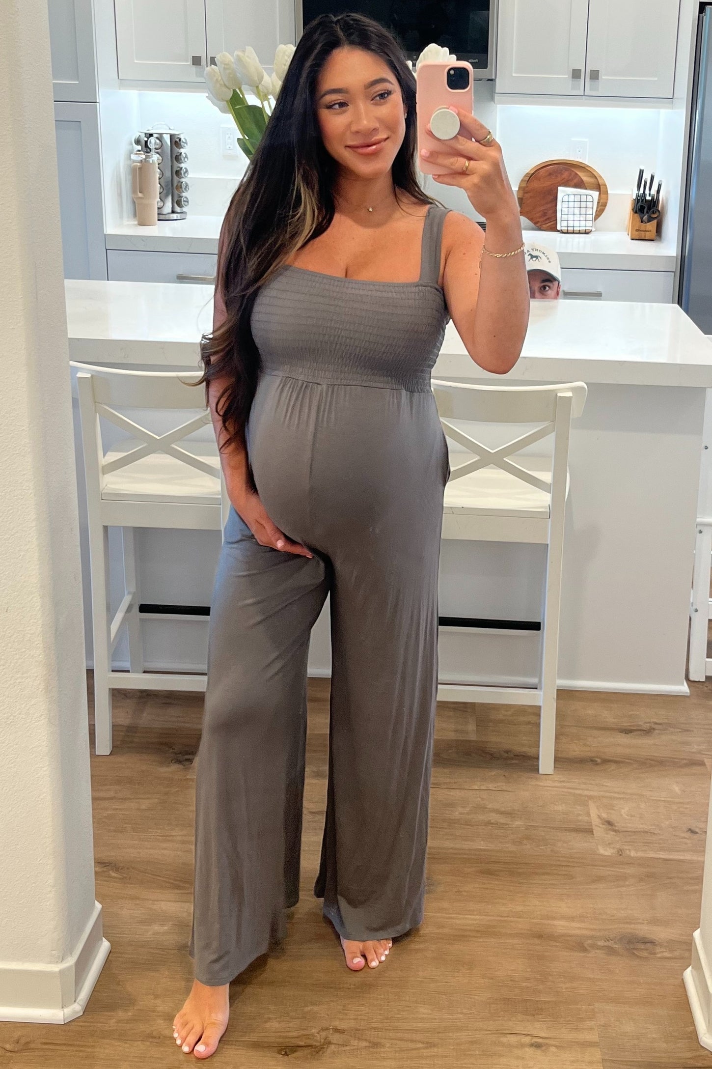 woman wearing a grey maternity jumpsuit with a smocked bodice and a visible baby bump