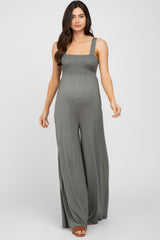 woman wearing a green maternity jumpsuit with a smocked bodice and wide legs, showcasing her baby bump