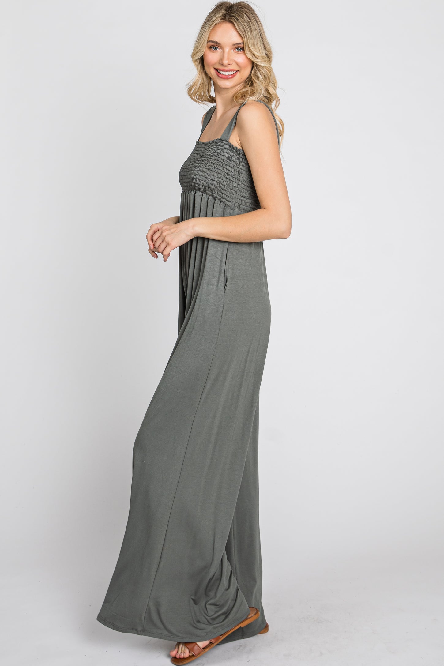 woman wearing a charcoal grey smocked wide leg jumpsuit with pockets and brown sandals