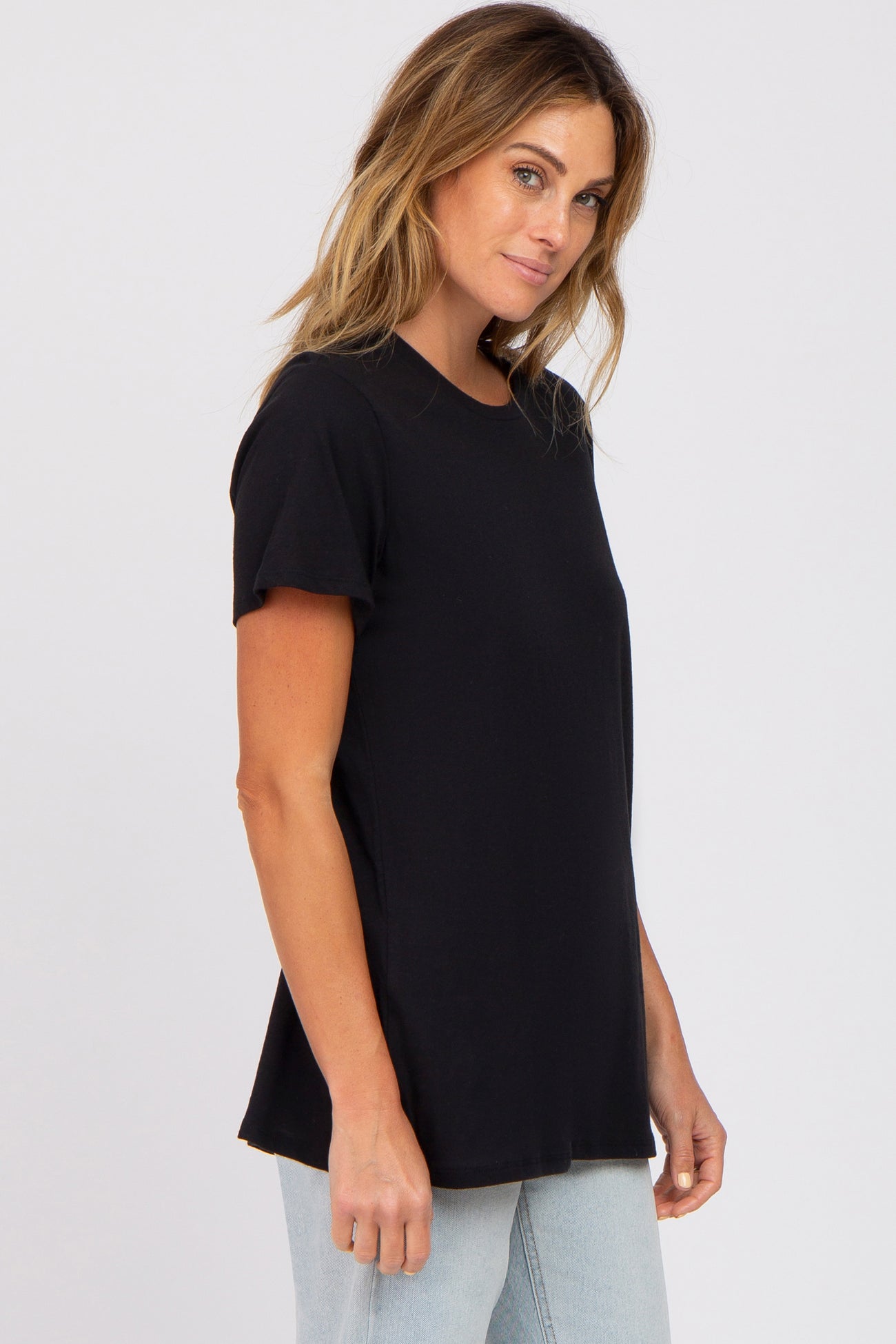 woman wearing a black short sleeve t-shirt paired with light blue jeans, standing sideways with a relaxed expression