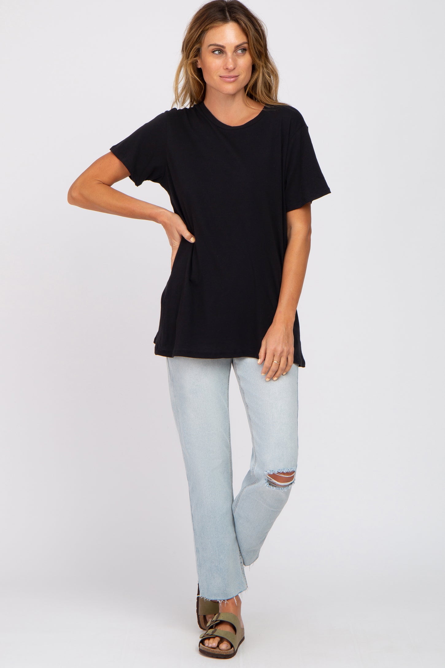 woman wearing a black short sleeve t-shirt and light blue distressed jeans, standing with one hand on her hip