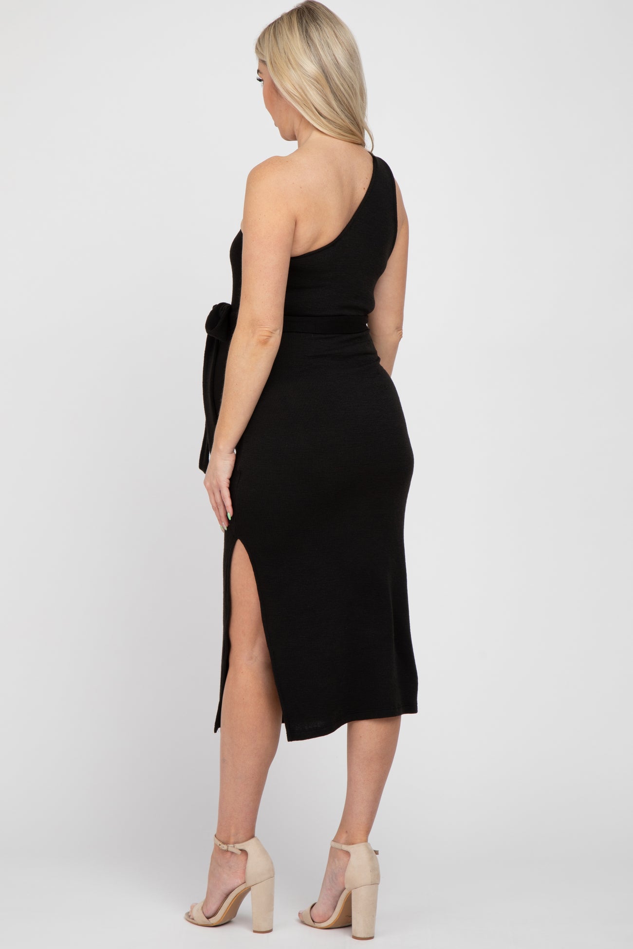 woman wearing a black one-shoulder ribbed maternity dress with a tie waist and side slit, showcasing her baby bump