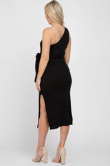 woman wearing a black one-shoulder ribbed maternity dress with a tie waist and side slit, showcasing her baby bump