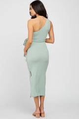 Woman from behind wearing a sage green one-shoulder ribbed midi dress with a waist tie and side slit