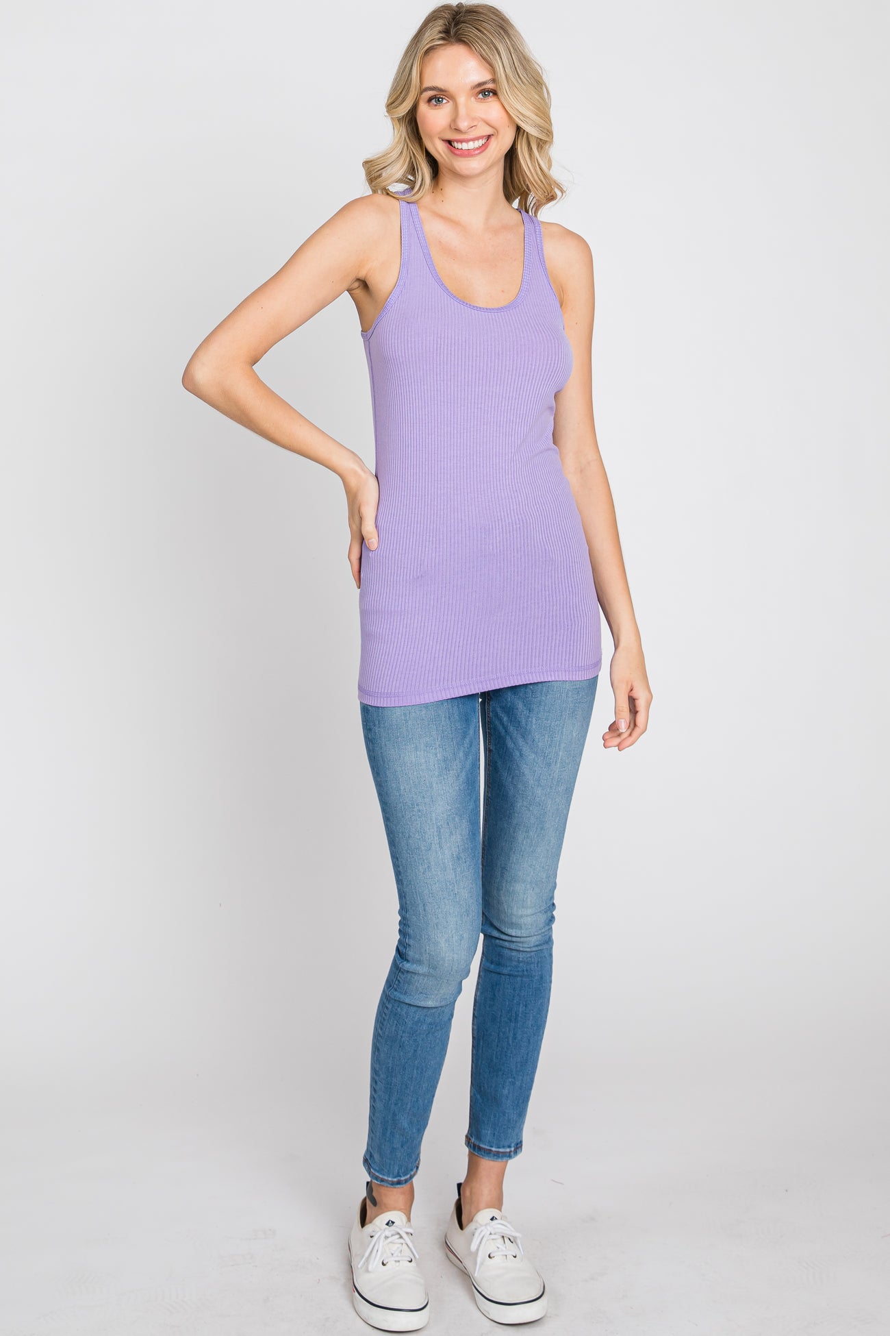 Woman wearing a purple ribbed tank top and blue skinny jeans with white sneakers
