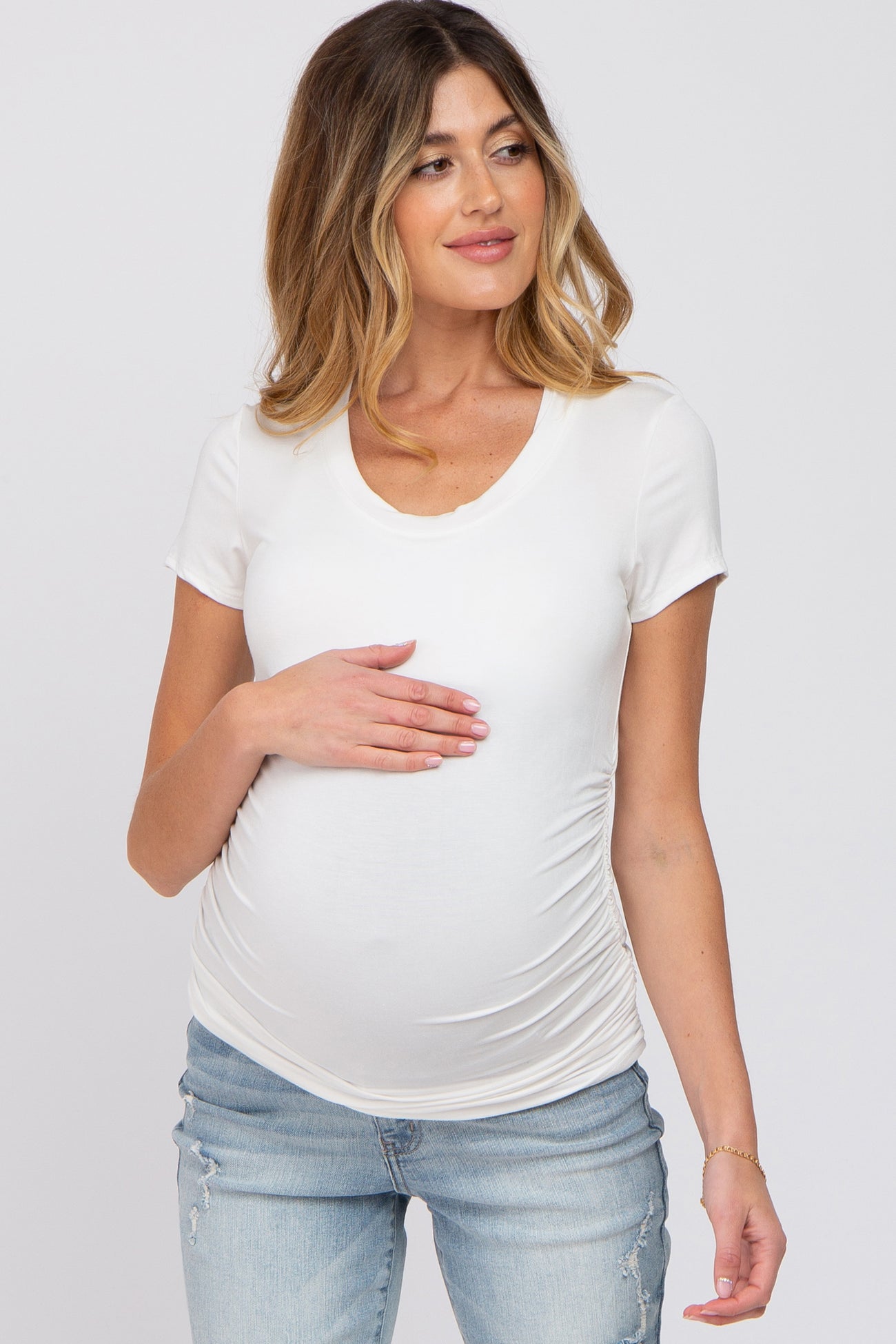 woman wearing a white short sleeve maternity top and holding her baby bump while smiling