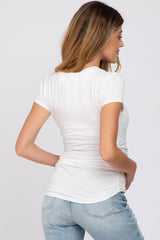 woman wearing a white short sleeve maternity top with ruched sides, showing a side view and holding her baby bump