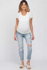woman wearing a white short sleeve maternity top and distressed light blue maternity jeans, highlighting her baby bump