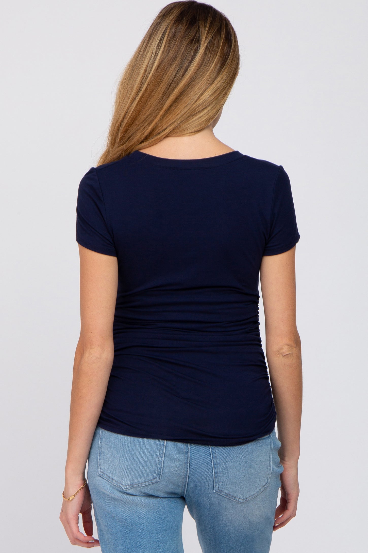 woman wearing a navy blue short sleeve maternity top with gathered details at the back and paired with light blue jeans