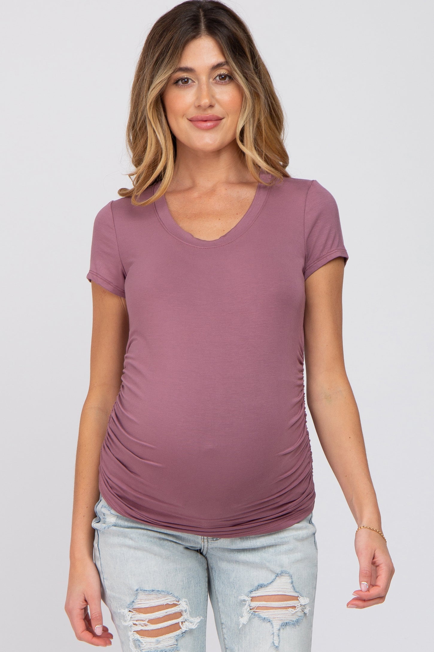 woman wearing a dusty mauve short sleeve maternity top with ruching and a visible baby bump, styled with distressed jeans