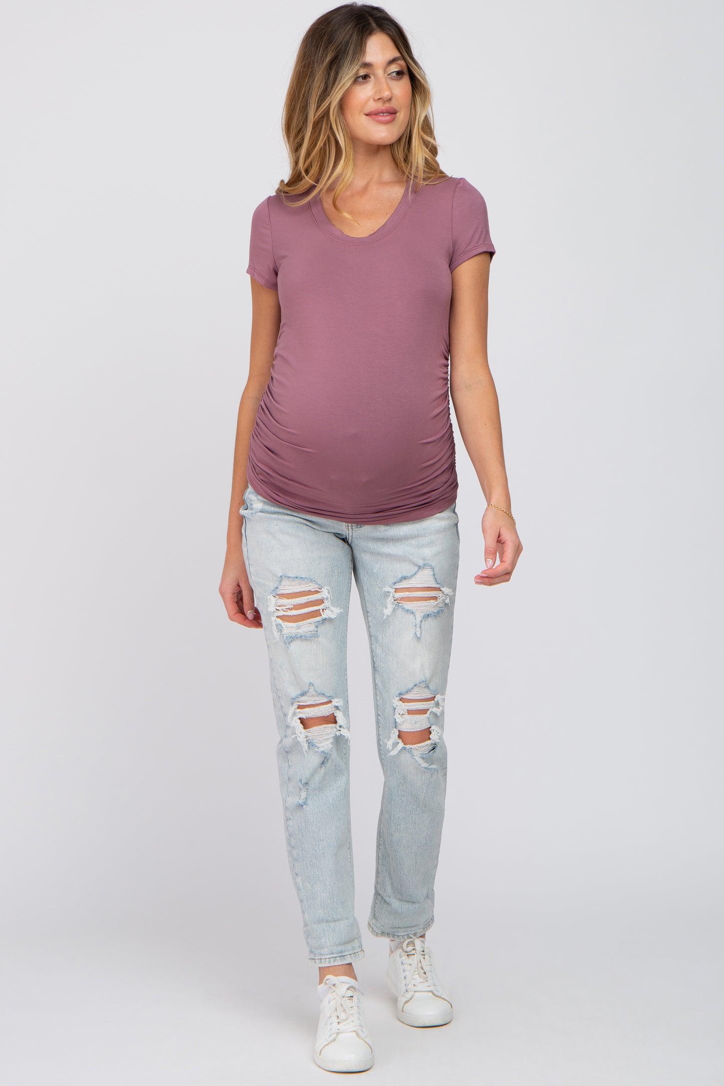 woman wearing a mauve v-neck maternity top and distressed light wash jeans, showing a baby bump
