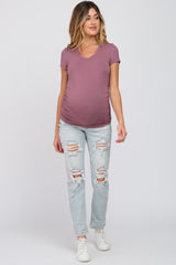 woman wearing a mauve v-neck maternity top and distressed light wash jeans, showing a baby bump