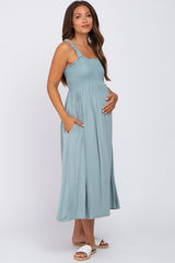 Pregnant woman wearing a light blue smocked maternity midi dress with pockets and ruffled straps