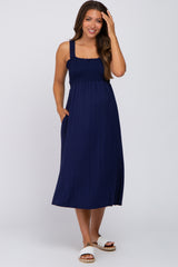 woman wearing a navy blue maternity dress with a smocked bodice and pockets, showing her baby bump