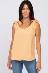 woman wearing a peach sleeveless top with bow details on the shoulders and paired with blue jeans
