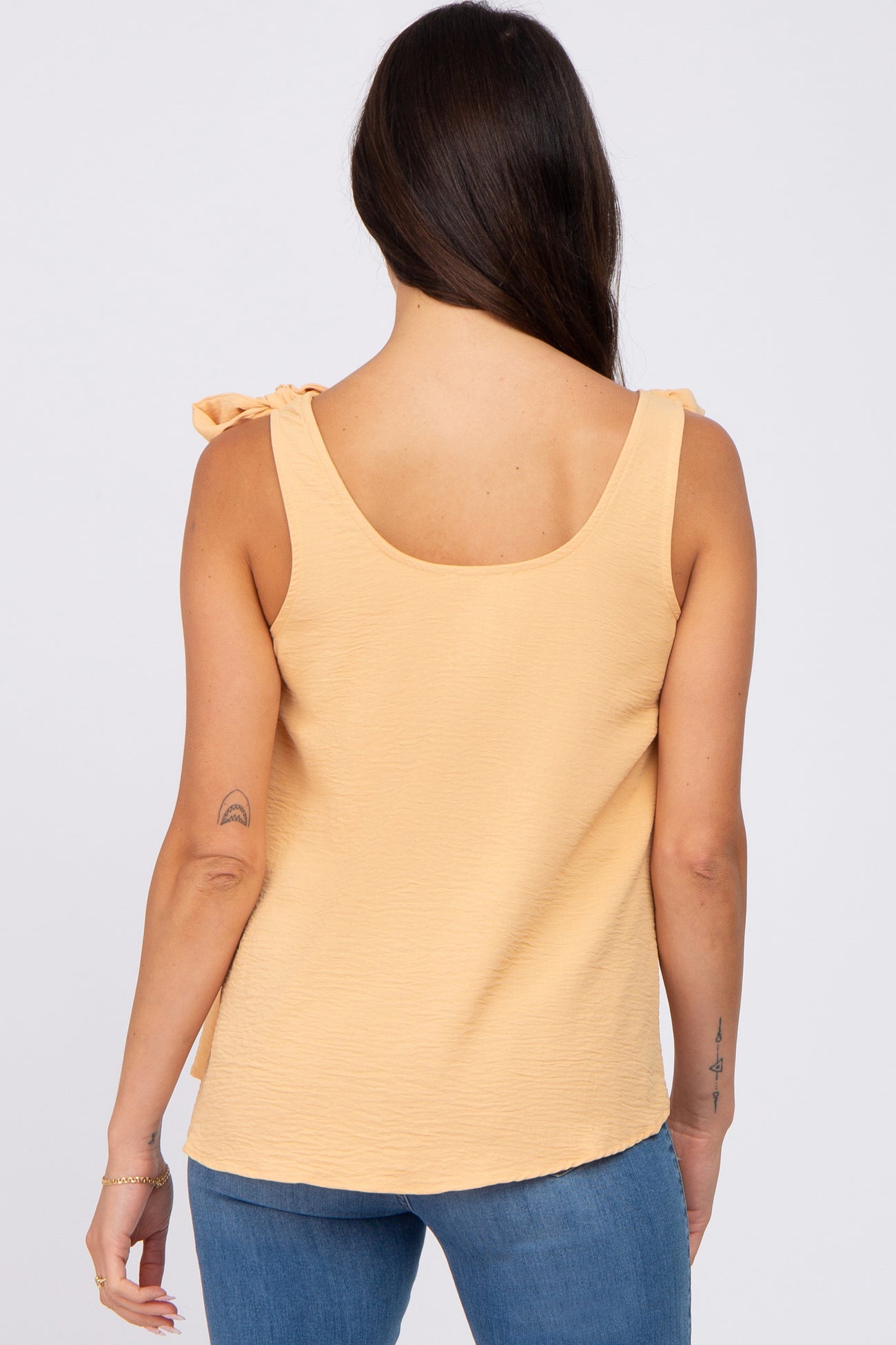 woman wearing a light yellow sleeveless top with bow tie details on the shoulders, viewed from the back