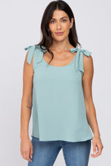 woman wearing a light blue sleeveless top with bow tie details on the shoulders and paired with denim jeans