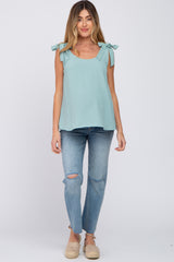 woman wearing a light teal maternity top with tie straps and paired with distressed jeans