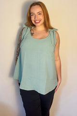 woman wearing a light green maternity top with tie straps and a relaxed fit, paired with black pants