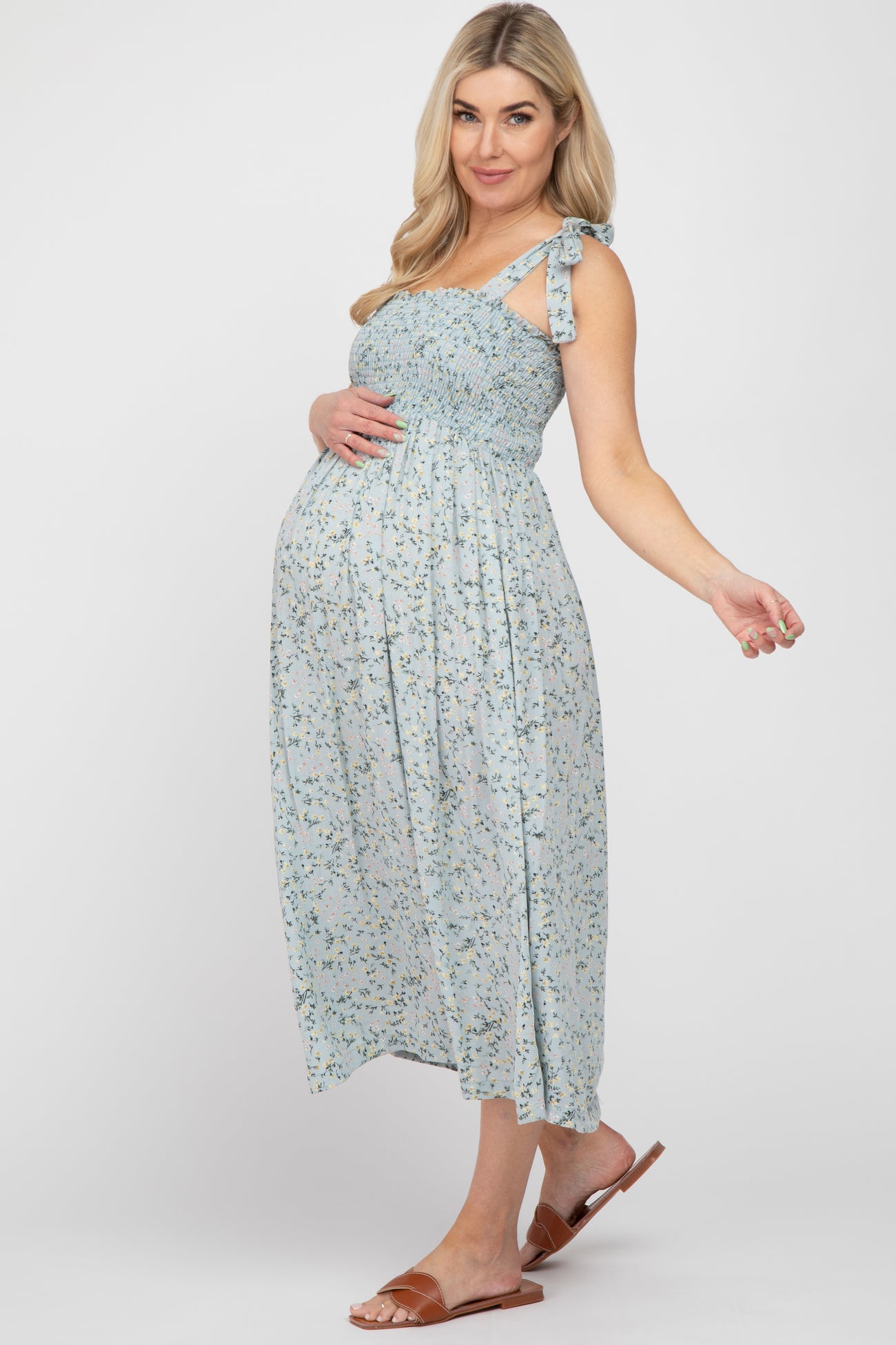 woman wearing a light blue floral maternity maxi dress with a smocked bodice and one adjustable tie strap, showcasing her baby bump