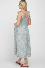 woman wearing a light blue floral maternity dress with tie straps and a smocked bodice, showing her baby bump from the back
