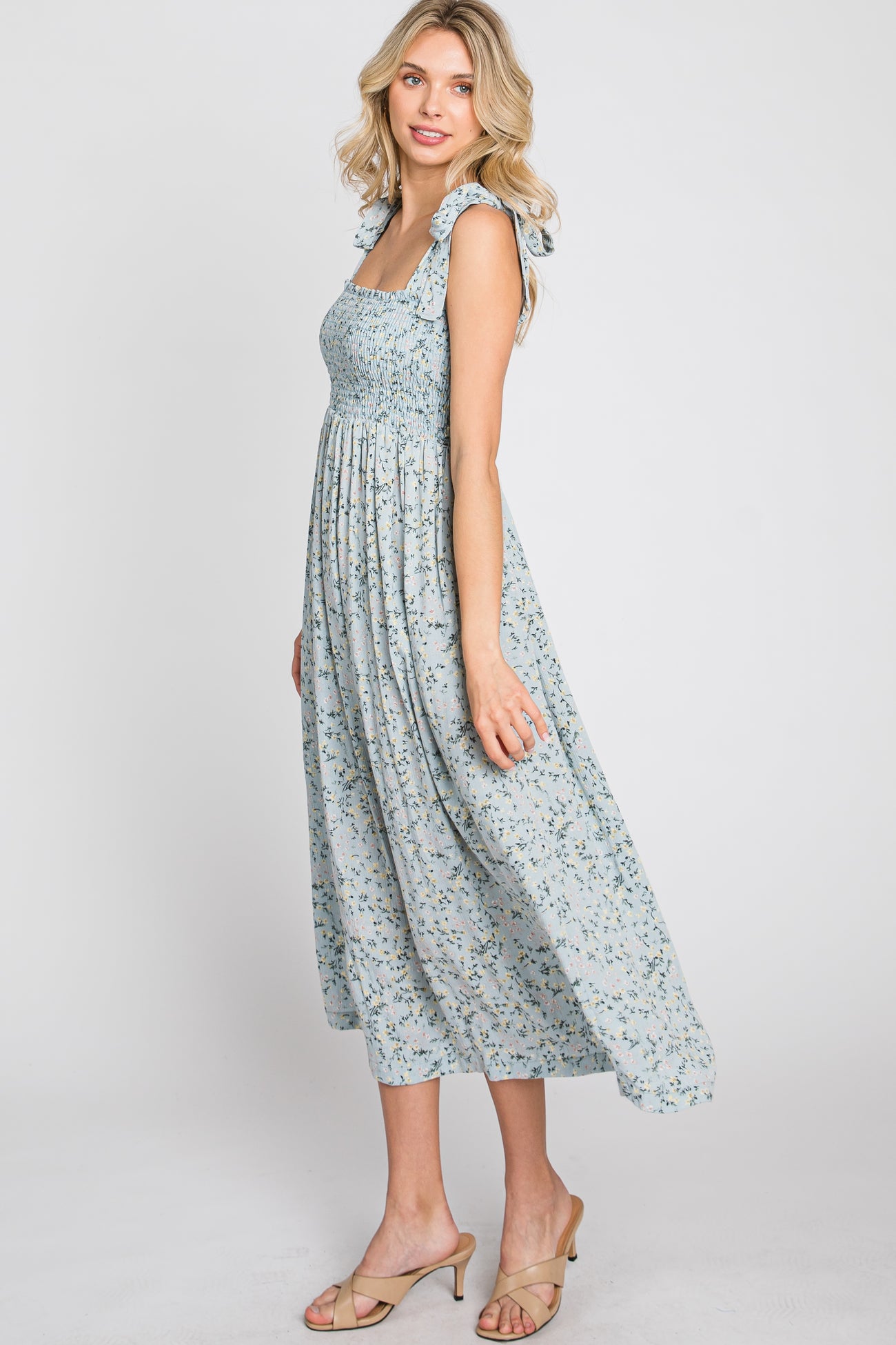woman wearing a light blue floral midi dress with smocked bodice and ruffle straps, standing in profile