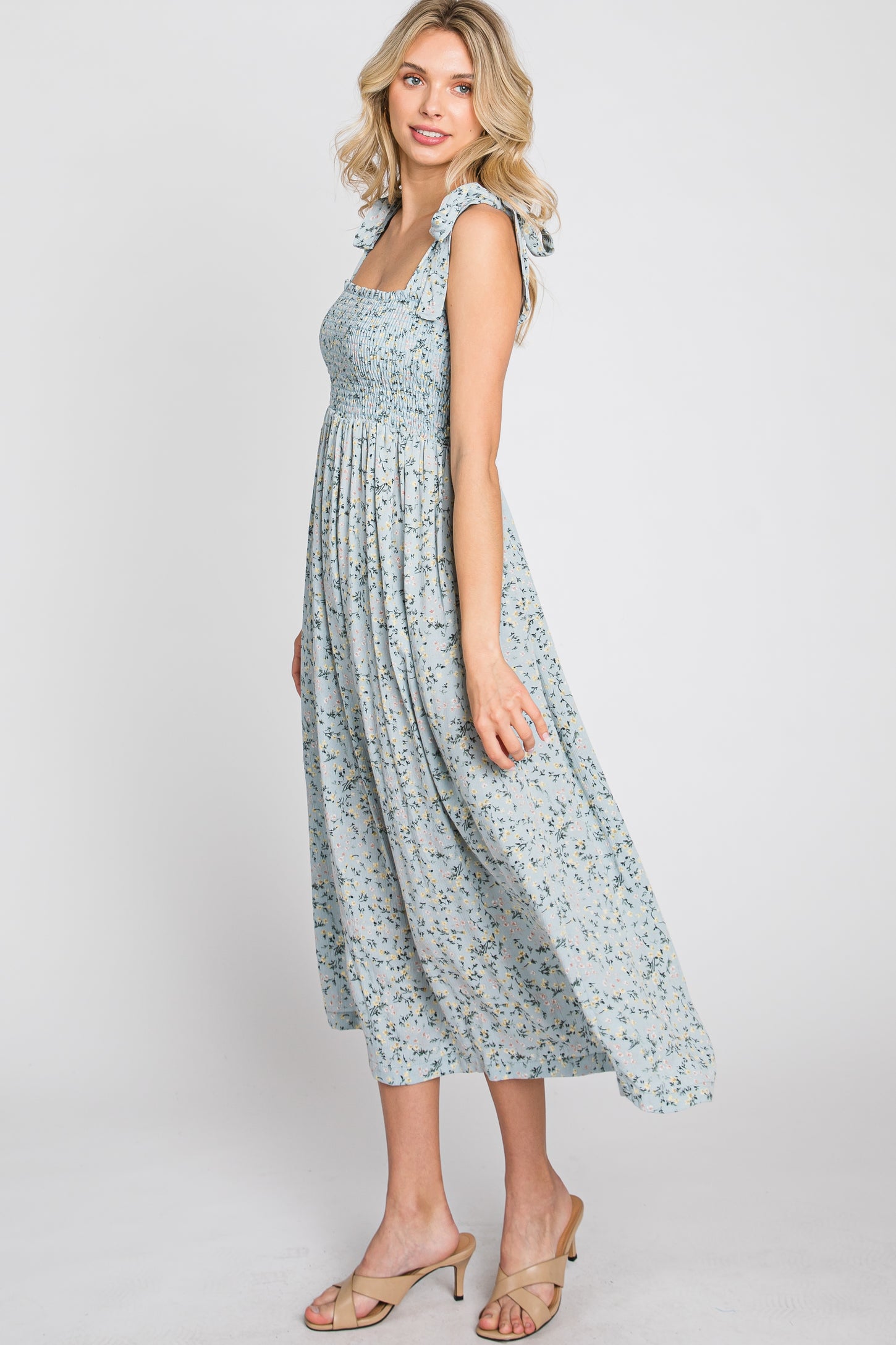 woman wearing a light blue floral midi dress with smocked bodice and ruffle straps, standing in profile