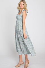woman wearing a light blue floral midi dress with smocked bodice and ruffle straps, standing in profile