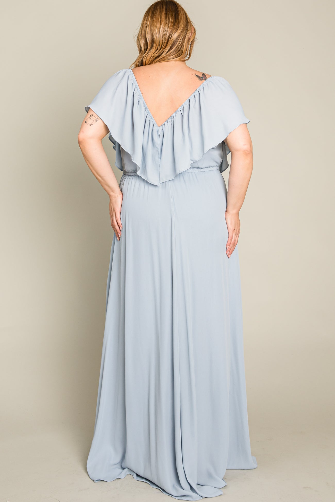 Back view of a woman wearing a light blue plus size maxi dress with a ruffled V-neckline and flowing skirt