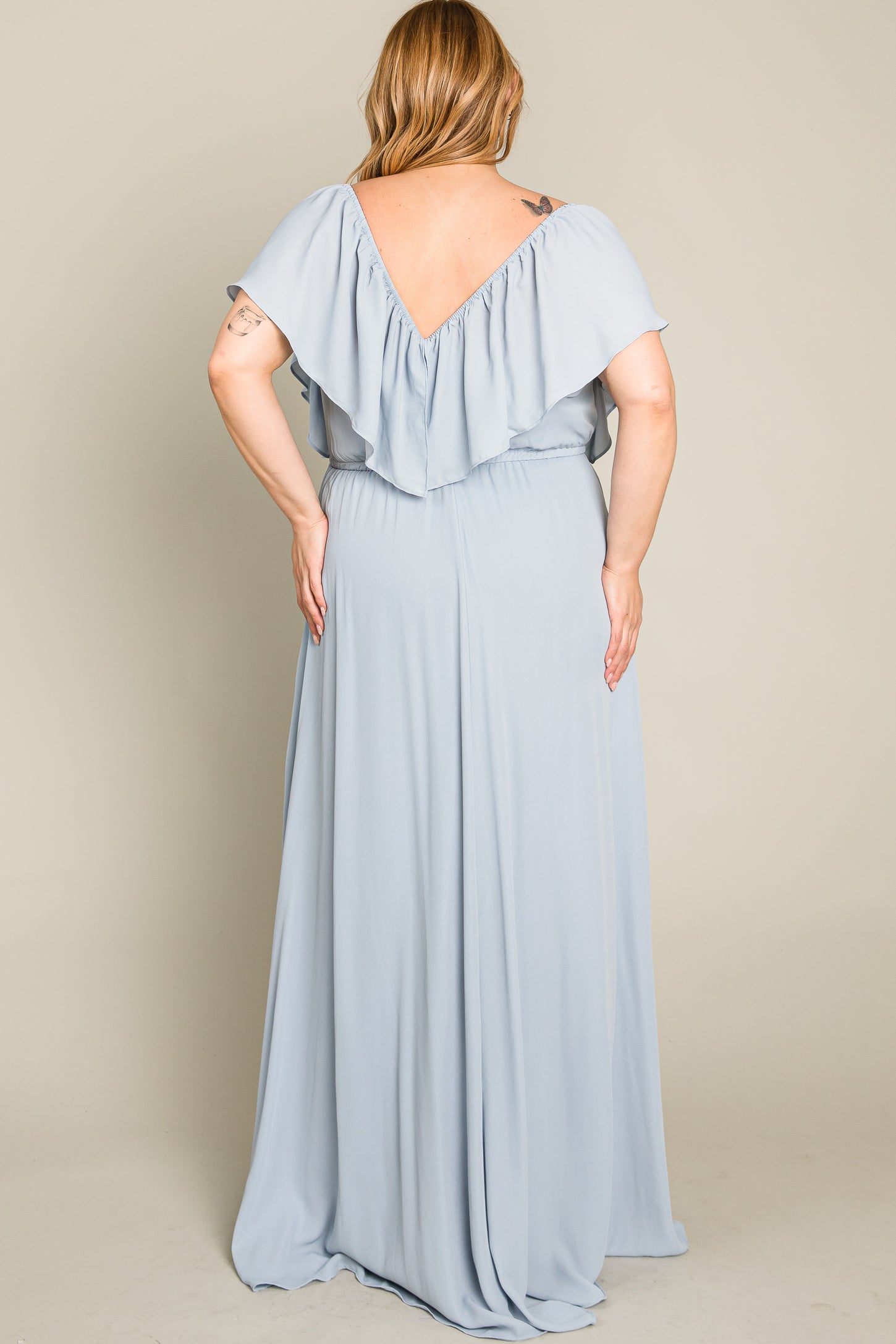 Back view of a woman wearing a light blue plus size maxi dress with a ruffled V-neckline and flowing skirt