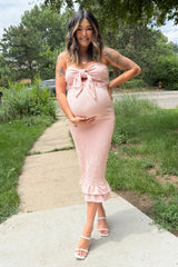 woman wearing a blush pink strapless maternity dress with a tie front and ruffled hem, showing her baby bump