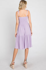 Back view of a woman wearing a lavender smocked midi dress with tie straps and tan wedge sandals