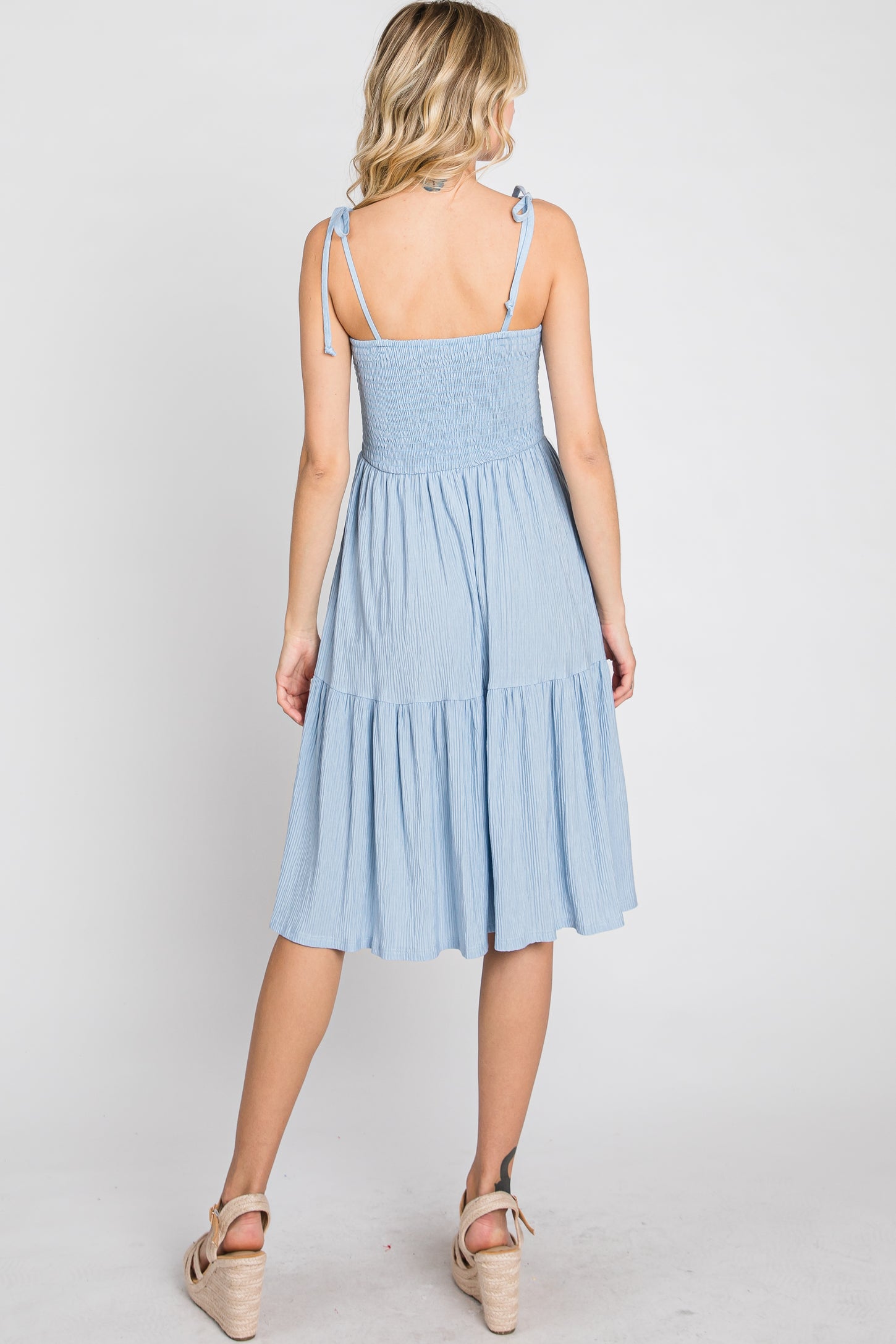 woman wearing a light blue smocked midi dress with adjustable straps and tiered skirt, viewed from the back