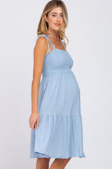 woman wearing a light blue maternity dress with a smocked bodice and tiered skirt, showing her baby bump