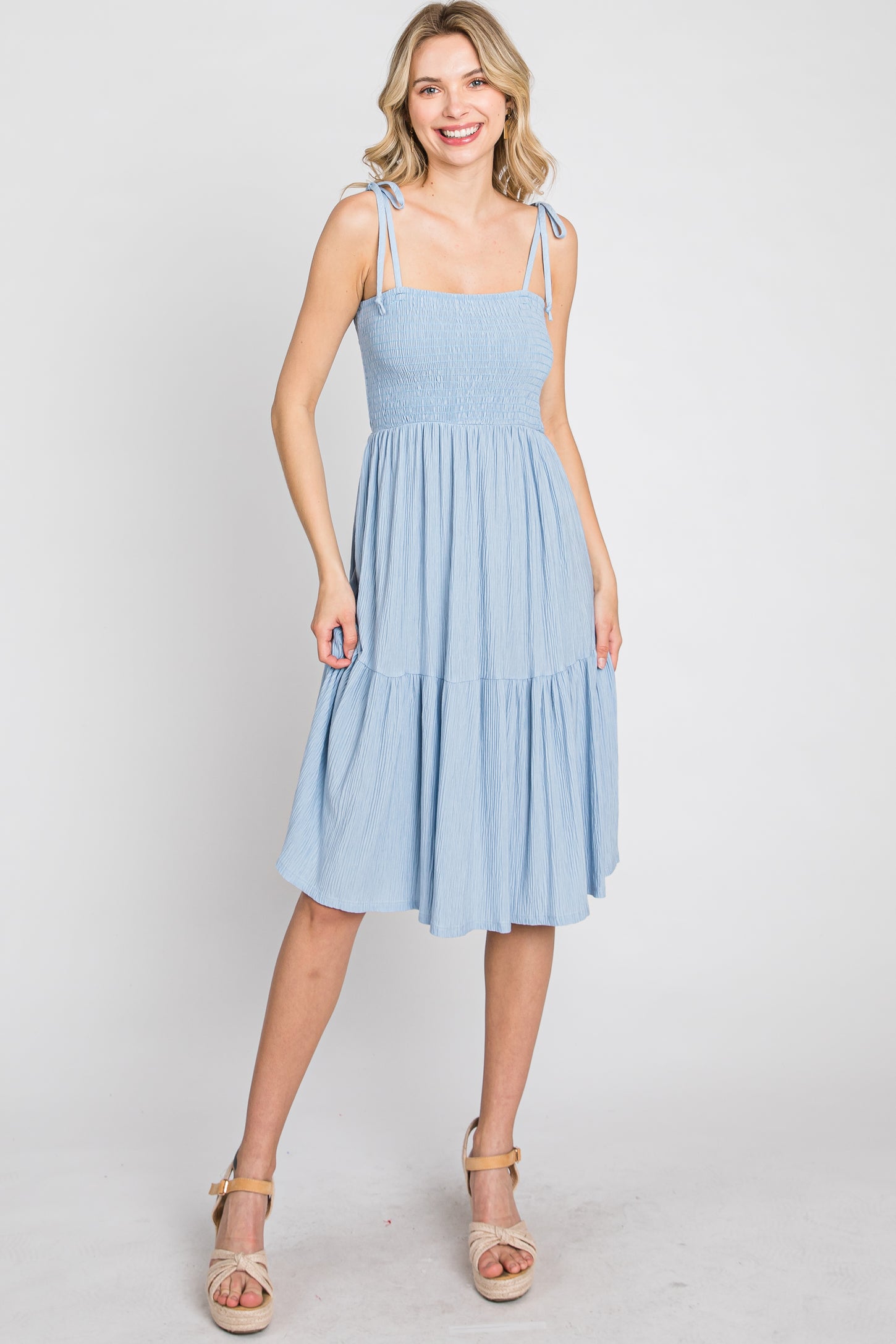 woman wearing a light blue tiered summer dress with adjustable tie straps and a smocked bodice