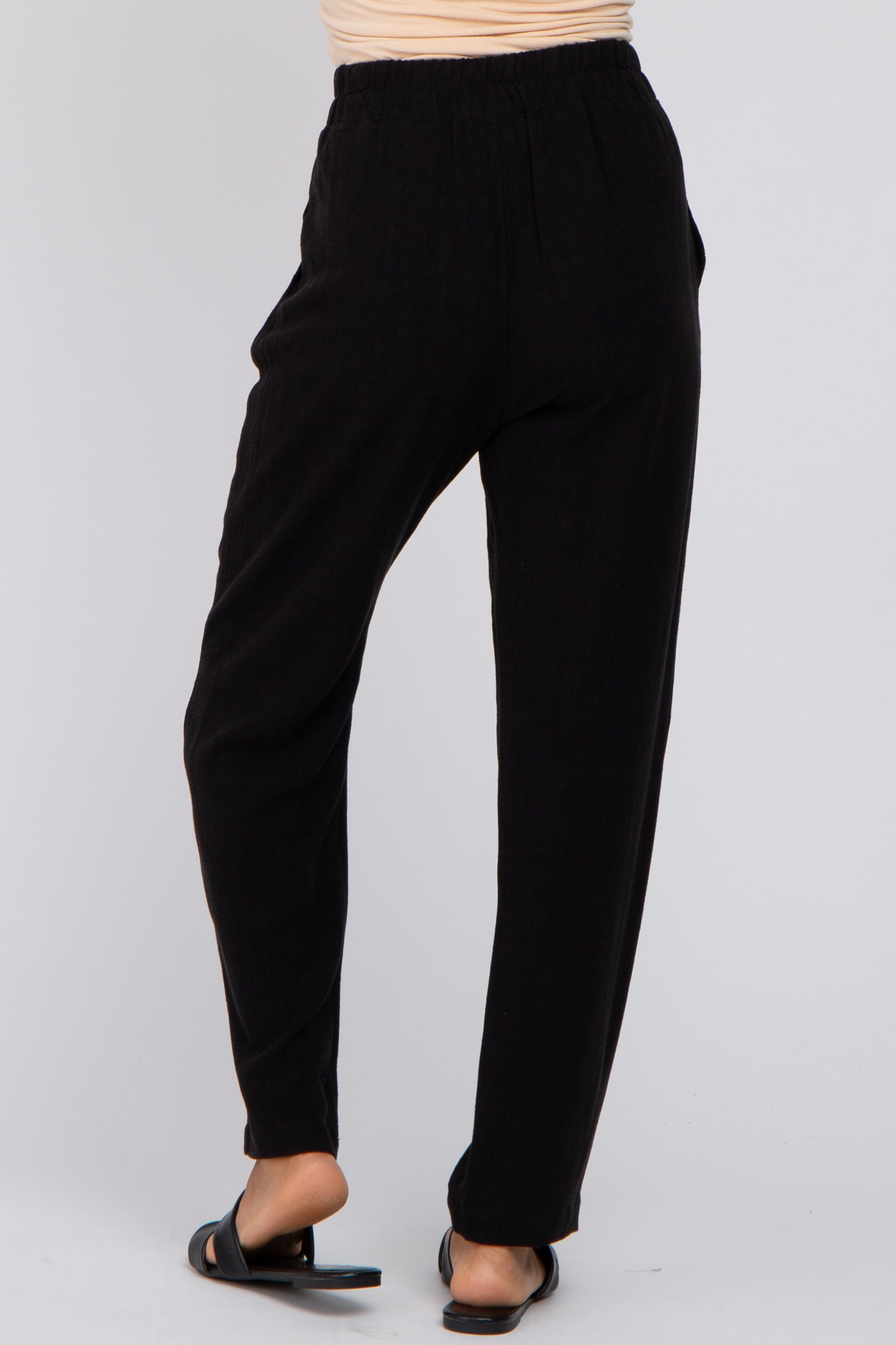woman wearing black loose-fitting high-waisted pants, shown from the back, paired with black slide sandals
