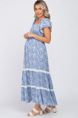 Pregnant woman wearing a blue floral smocked maternity maxi dress with white lace trim and short sleeves