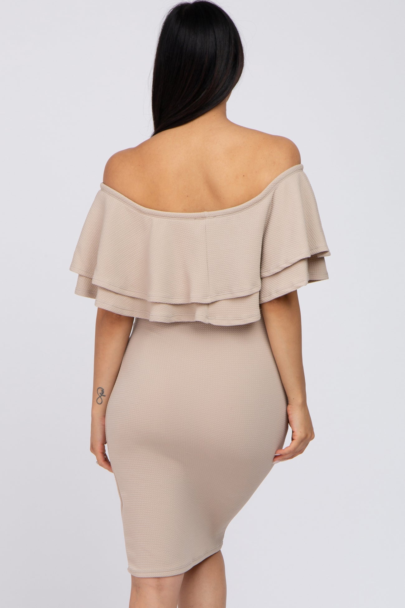woman wearing a beige off-the-shoulder maternity dress with layered ruffle details and a fitted silhouette
