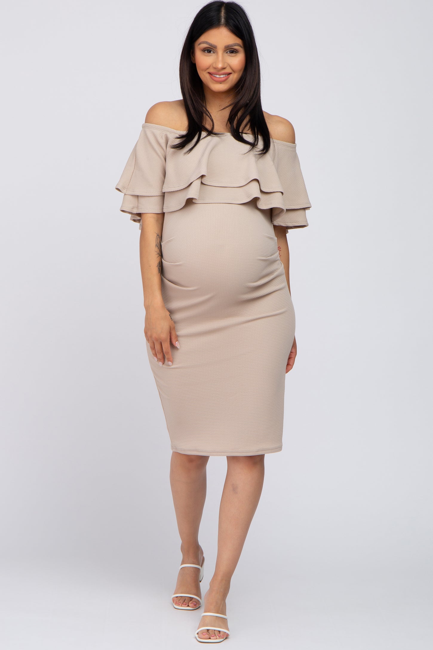 woman wearing a beige off-shoulder maternity dress with ruffle details and a visible baby bump