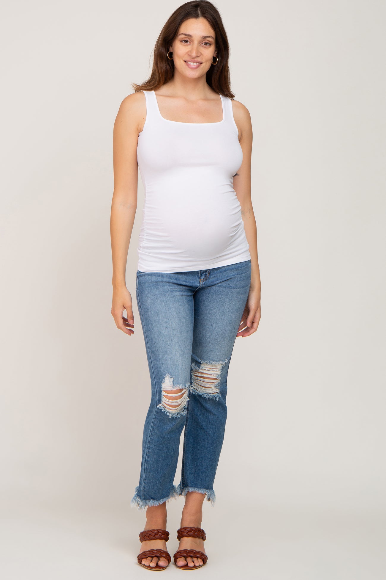 woman wearing a white maternity tank top and distressed blue jeans, showing her baby bump